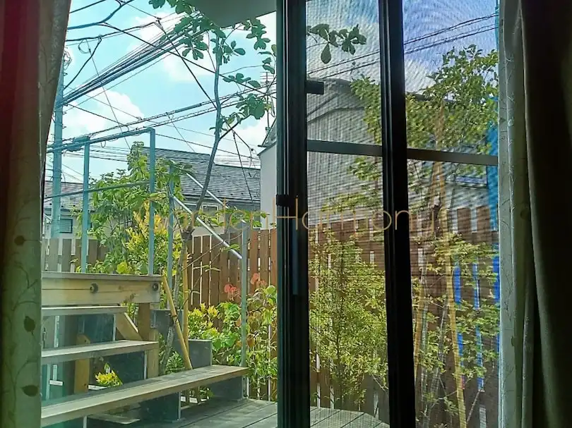 小さな雑木の庭 風が流れる緑の小道｜埼玉県のガーデンハーモニー・部屋の中の窓辺から見た庭の写真・ウッドフェンスを背景に見える雑木の庭の様子